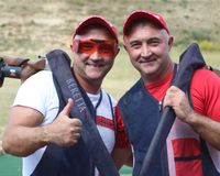 Zwei Flinten-Schützen blicken in die Kamera und machen die "Daumen hoch" Geste. Ihre Sportgeräte haben sie über die Schultern gelegt.