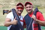 Zwei Flinten-Schützen blicken in die Kamera und machen die "Daumen hoch" Geste. Ihre Sportgeräte haben sie über die Schultern gelegt.