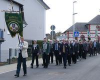 Ein Fahnenträger in weißer Jacke vor einer festlichen Marschgruppe, die als Delegation beim Festumzug teilnahm.