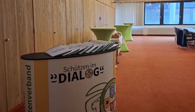 Blick in einen Raum mit einer Theke, auf der Logo des Projekts "Schützen im Dialog" zu sehen ist.