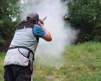 Ein Flintenschütze im Wettkampf. Pulverdampf, im Hintergrund eine zerspringende Wurfscheibe.